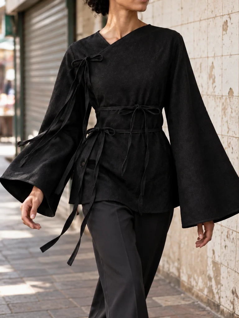 A fashion photograph of the exact black asymmetric top from the reference, showing its wide flared s