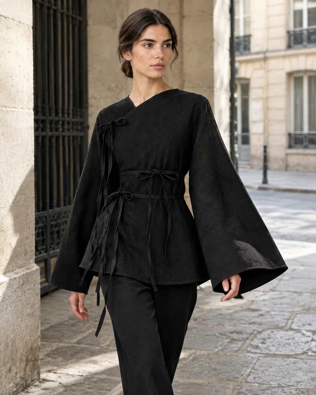 A fashion photograph of the exact black asymmetric wrap top from the reference, with its slanted nec