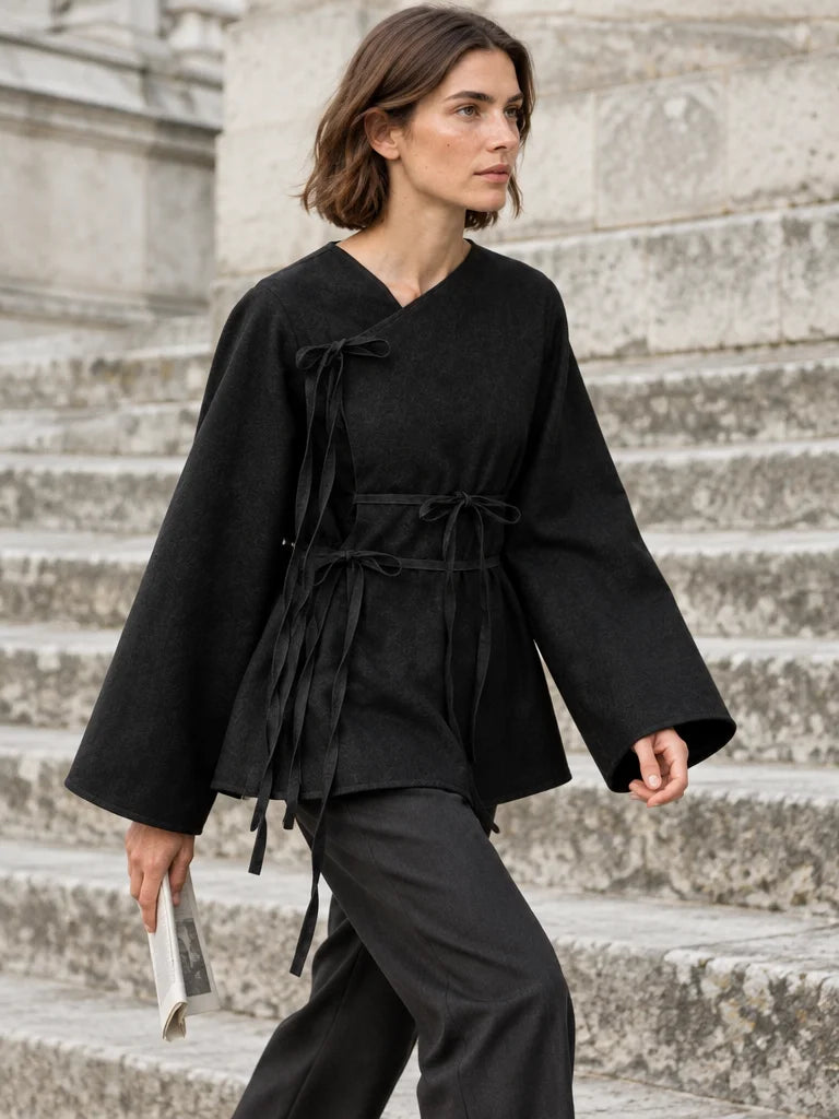 A fashion photograph of the exact black asymmetric wrap top from the reference, with the slanted nec